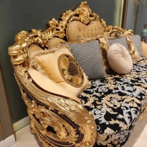 Home 39 A close-up view of the opulent gold carved details on the arm and back of a European style luxury sofa, showcasing the intricate gold leaf and the black and gold damask upholstery with varied accent pillows.